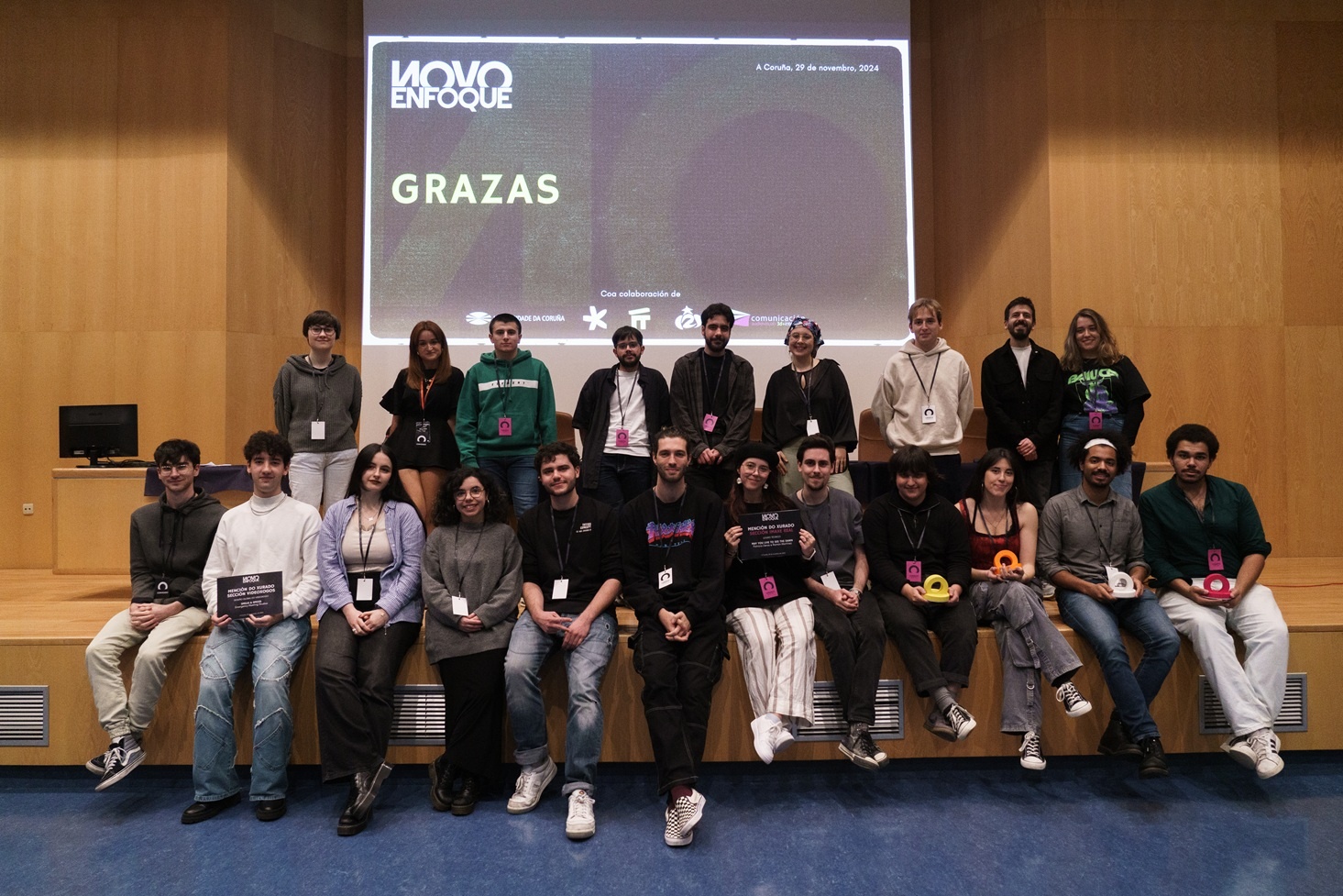 os mozos e mozas galardoados xunto con integrantes da organización ao remate da gala de entrega de premios do I Festival Novo Enfoque que tivo lugar, o pasado mes de novembro, na Facultade de Ciencias da Comunicación, no Campus da Coruña. Imaxe cedida pola organización do Festival Novo Enfoque.