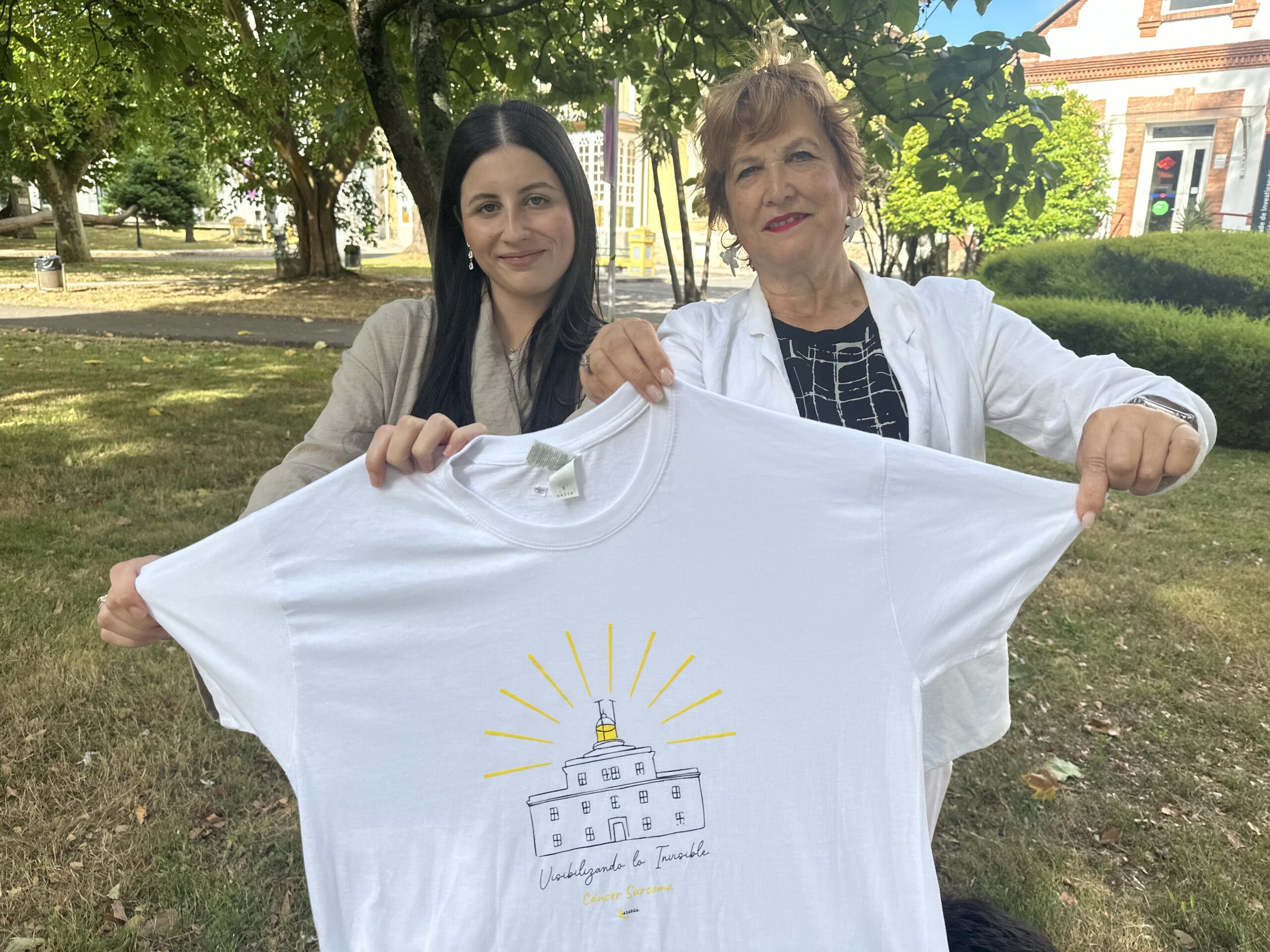 Clara Souto Ferreiro, alumna do grao en Xestión Industrial da Moda, e Mayte Deus Trasobares, presidenta de ASARGA, coa camiseta conmemorativa do Día Internacional do Sarcoma, nos xardíns do Campus Industrial de Ferrol